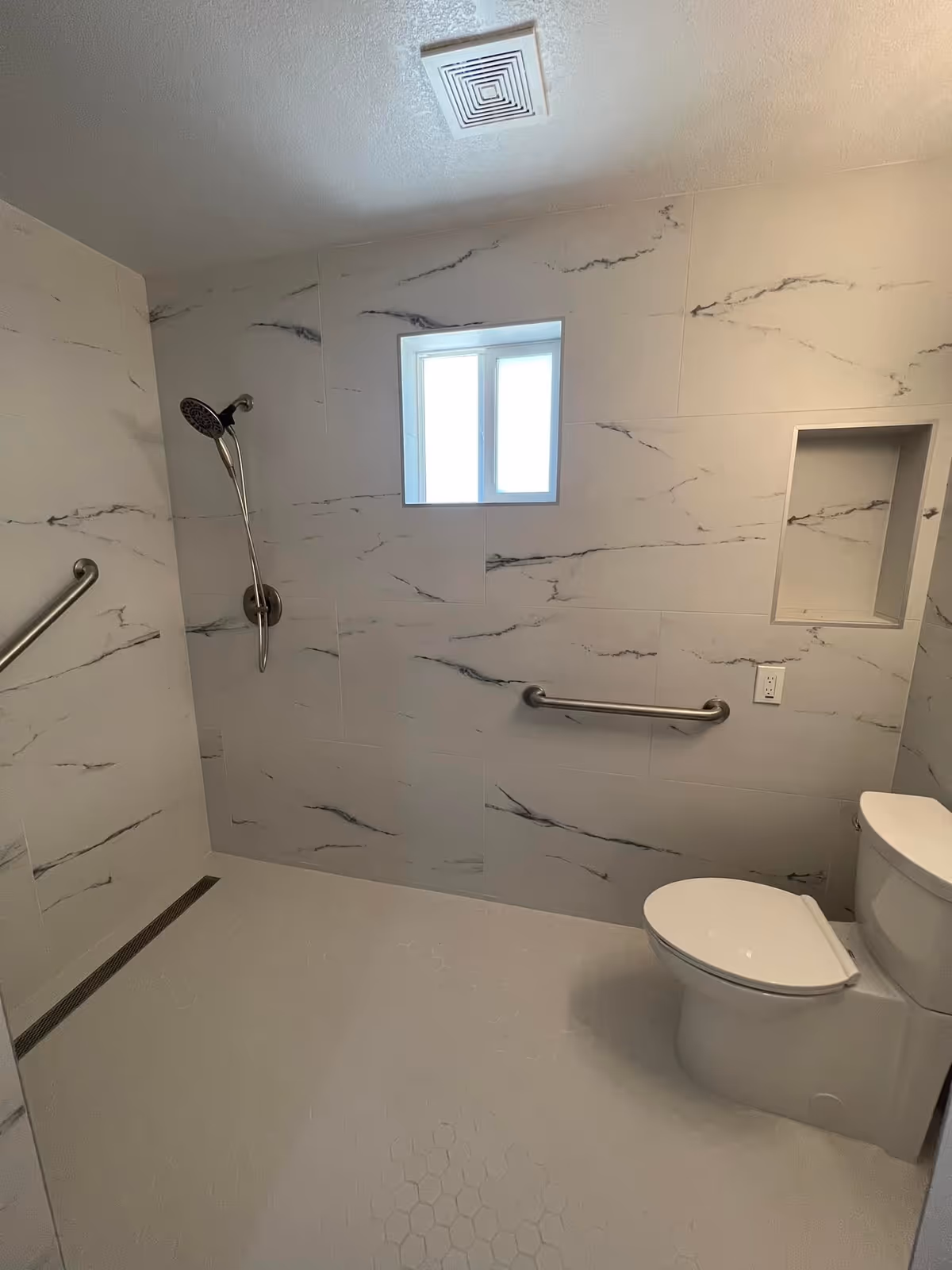 Accessible bathroom with a walk-in shower, handheld showerhead, grab bars, toilet, and a small window.