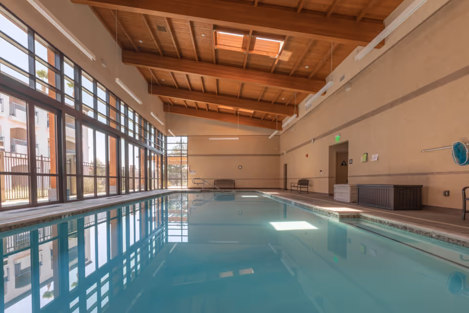 Indoor swimming pool in a high-ceilinged room with large windows and exposed wooden beams.