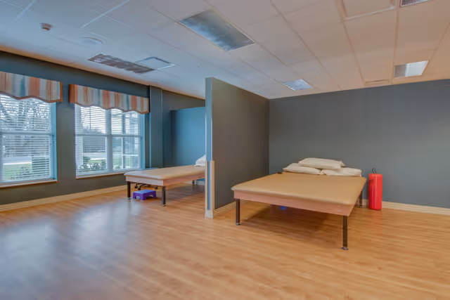 Spacious interior rehab/therapy room with two low treatment beds separated by a partial divider, wood floors and large windows.