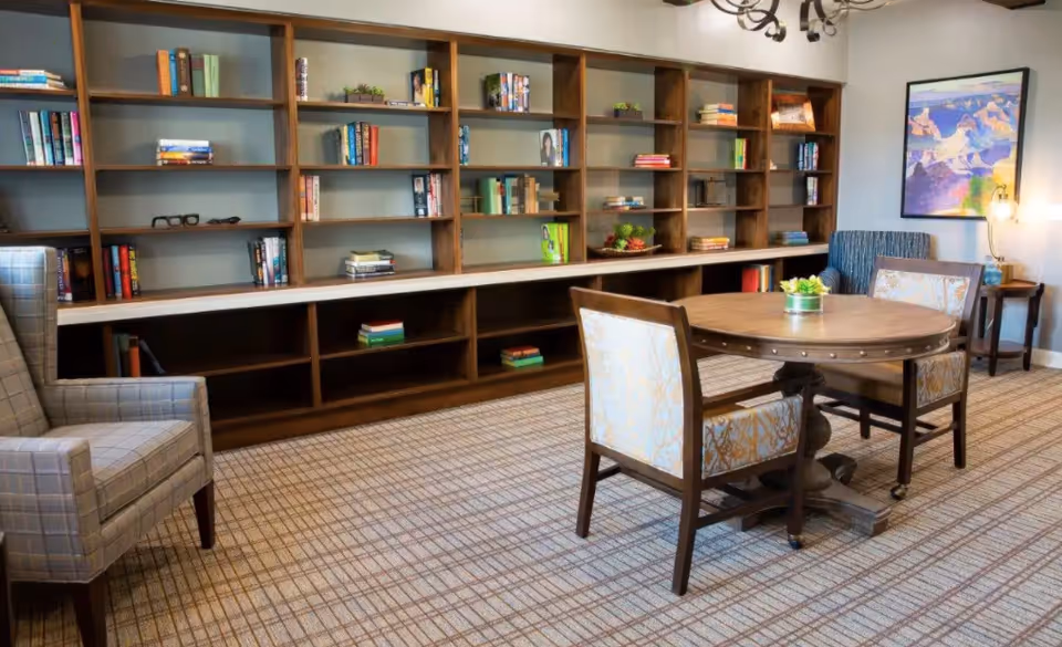 Cozy communal lounge with built-in bookshelves, a round wooden table and upholstered chairs.