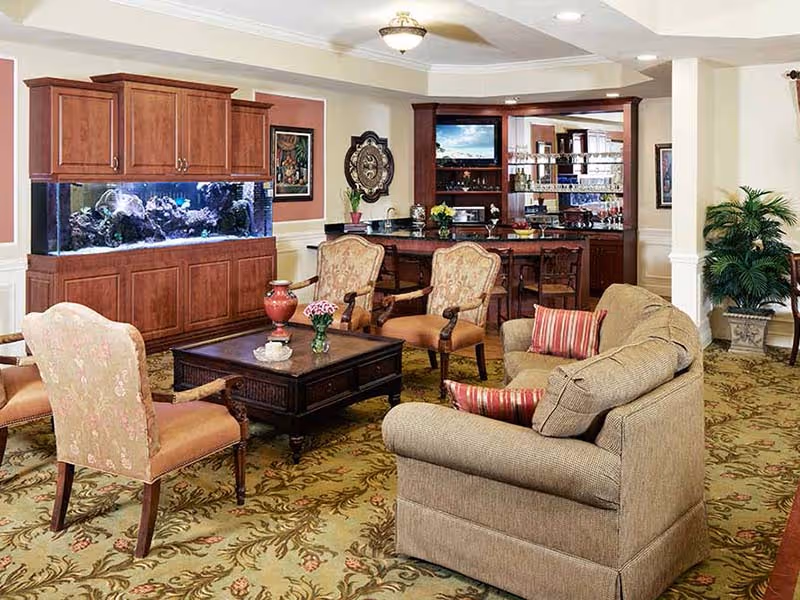 Comfortable lounge with sofas and armchairs around a coffee table, a large built-in aquarium to the left and a small bar area in the background.