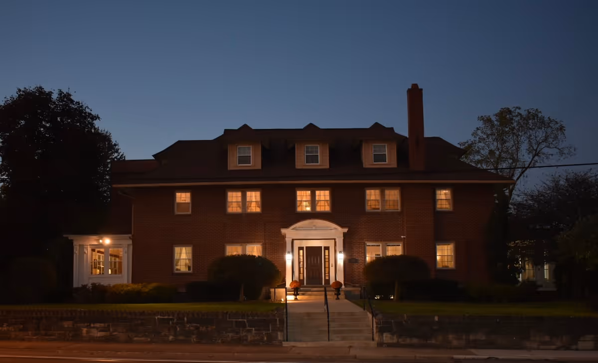 Brick multi-story building with warmly lit windows and a central entrance with steps at dusk.