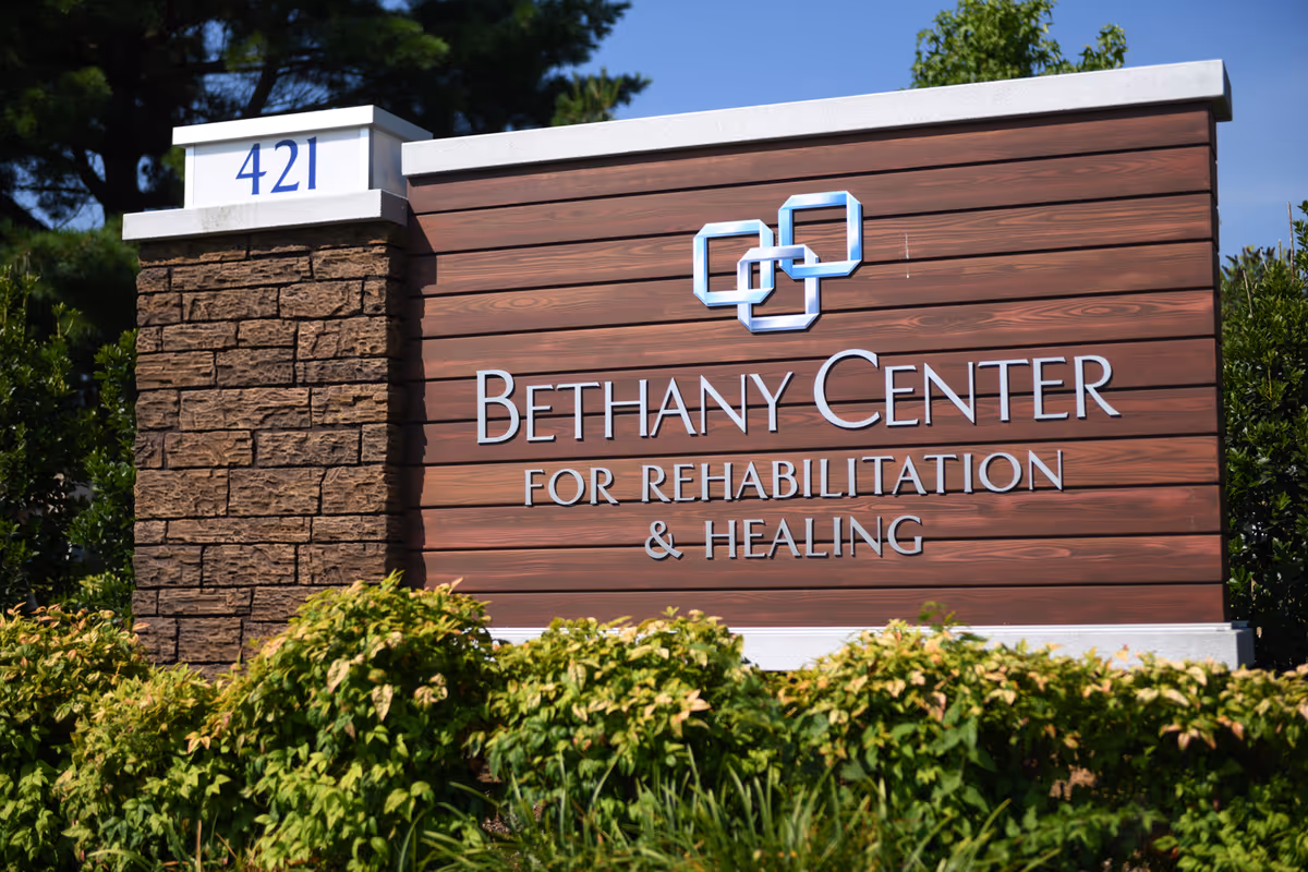Outdoor sign for Bethany Center for Rehabilitation & Healing with the address number 421 displayed on a stone and wood panel structure surrounded by greenery.