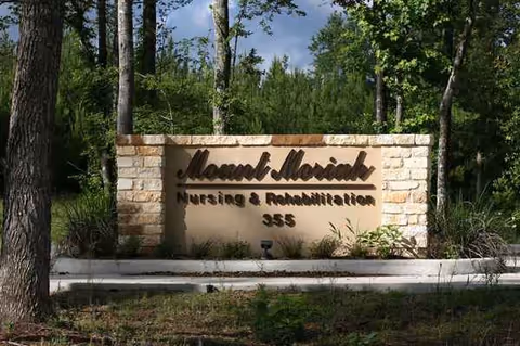 Stone entrance sign for a nursing and rehabilitation facility, with surrounding trees.