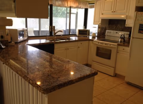Bright granite kitchen with sink, stove, white cabinets, and large windows.