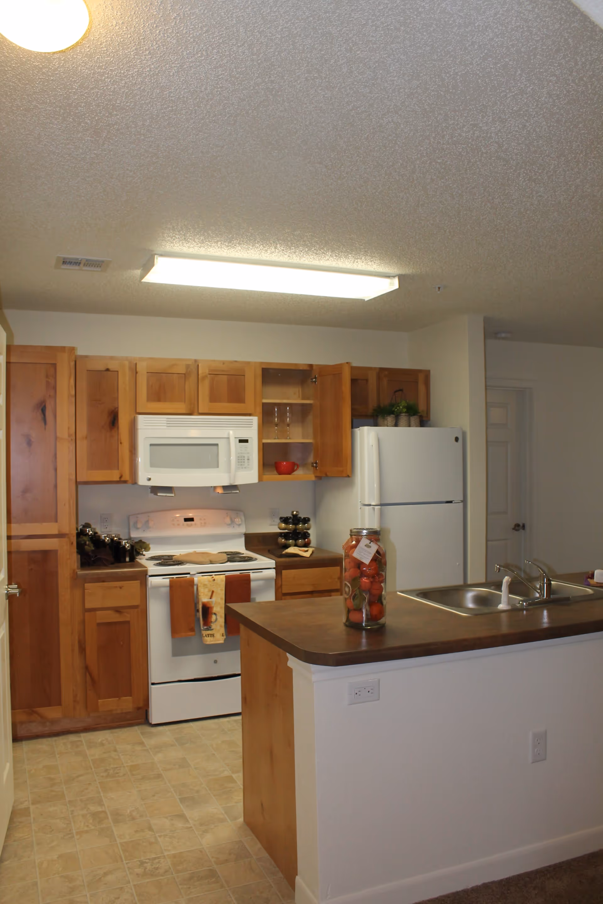 Small kitchen with wooden cabinets, white appliances, and a countertop island with a sink and decorative jar.