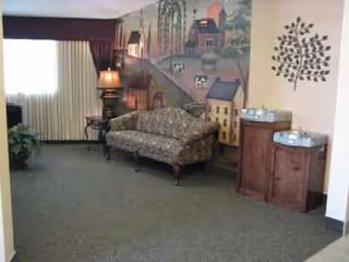 Cozy living area with a patterned sofa, lamp, and mural in a senior facility.