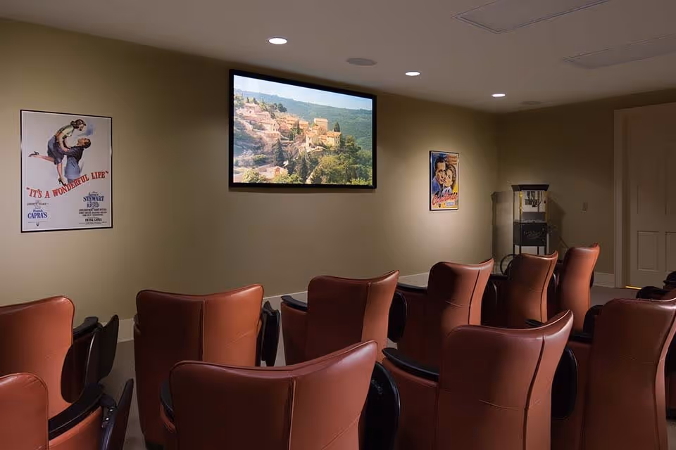 Small screening room with rows of red leather chairs facing a wall-mounted screen and vintage movie posters on the walls.