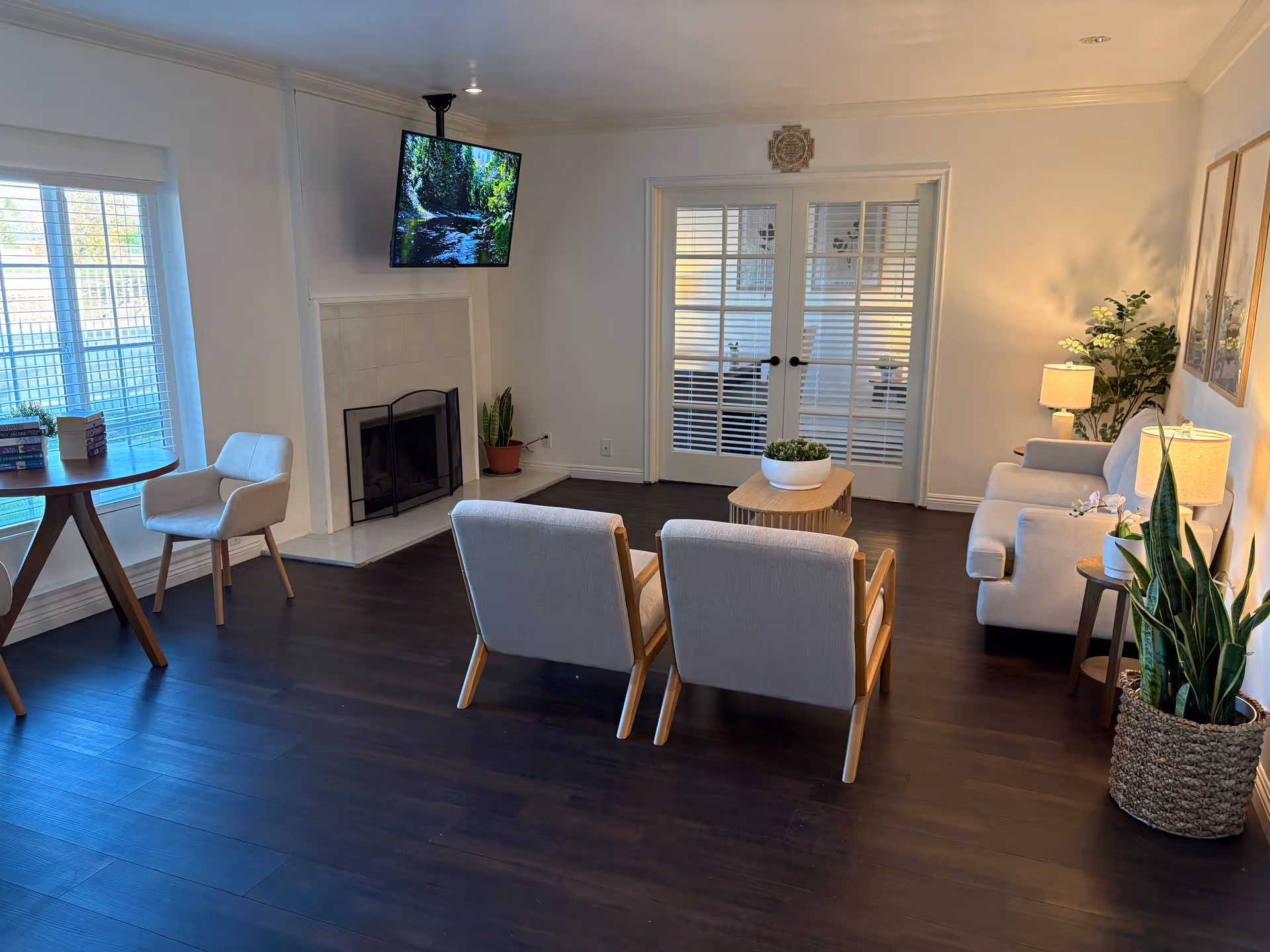 Bright lounge with chairs, a sofa, coffee table, fireplace, wall-mounted TV, and plants.