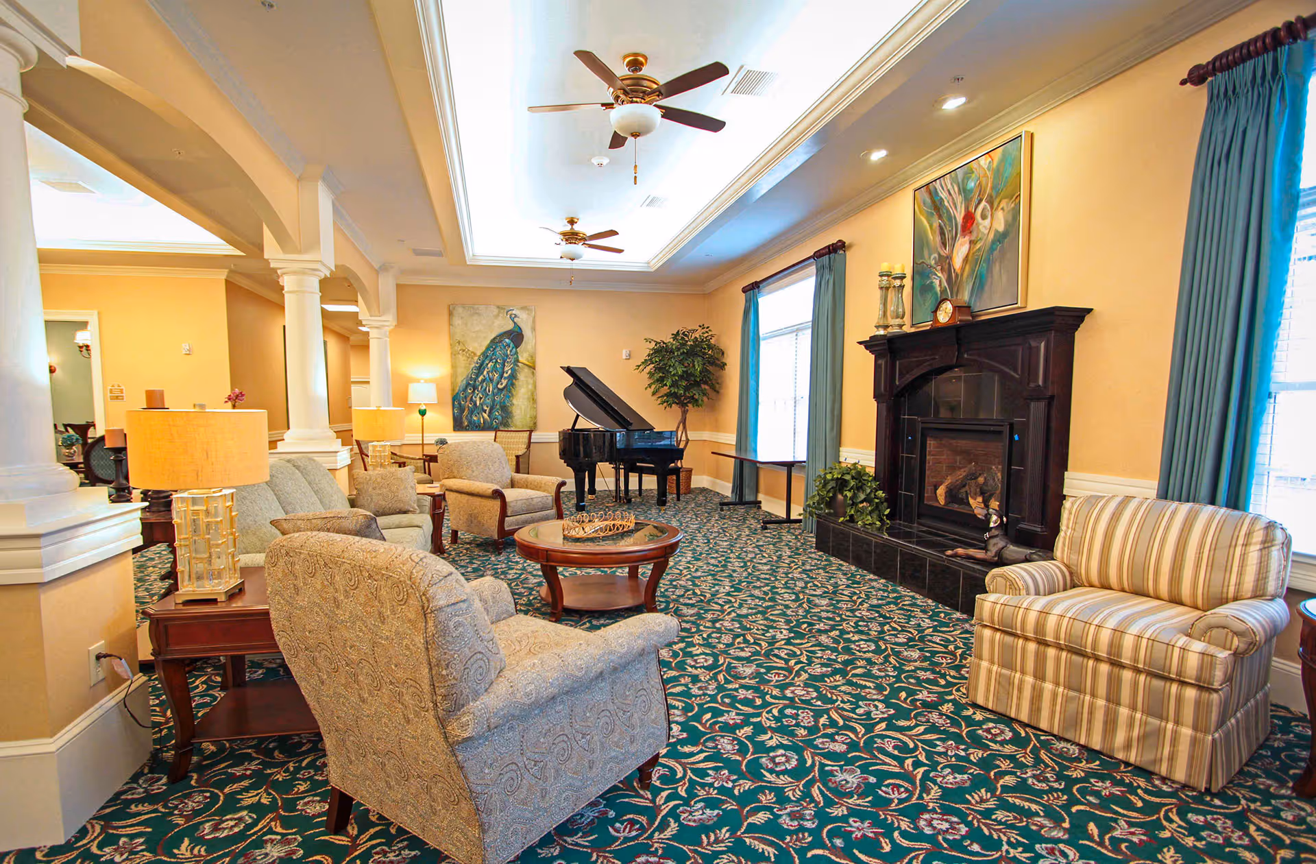 Bright communal living room with upholstered chairs, a fireplace, a grand piano, and patterned carpet.