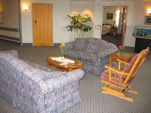 Senior living lounge with patterned sofas, a rocking chair, coffee table, and a plant.