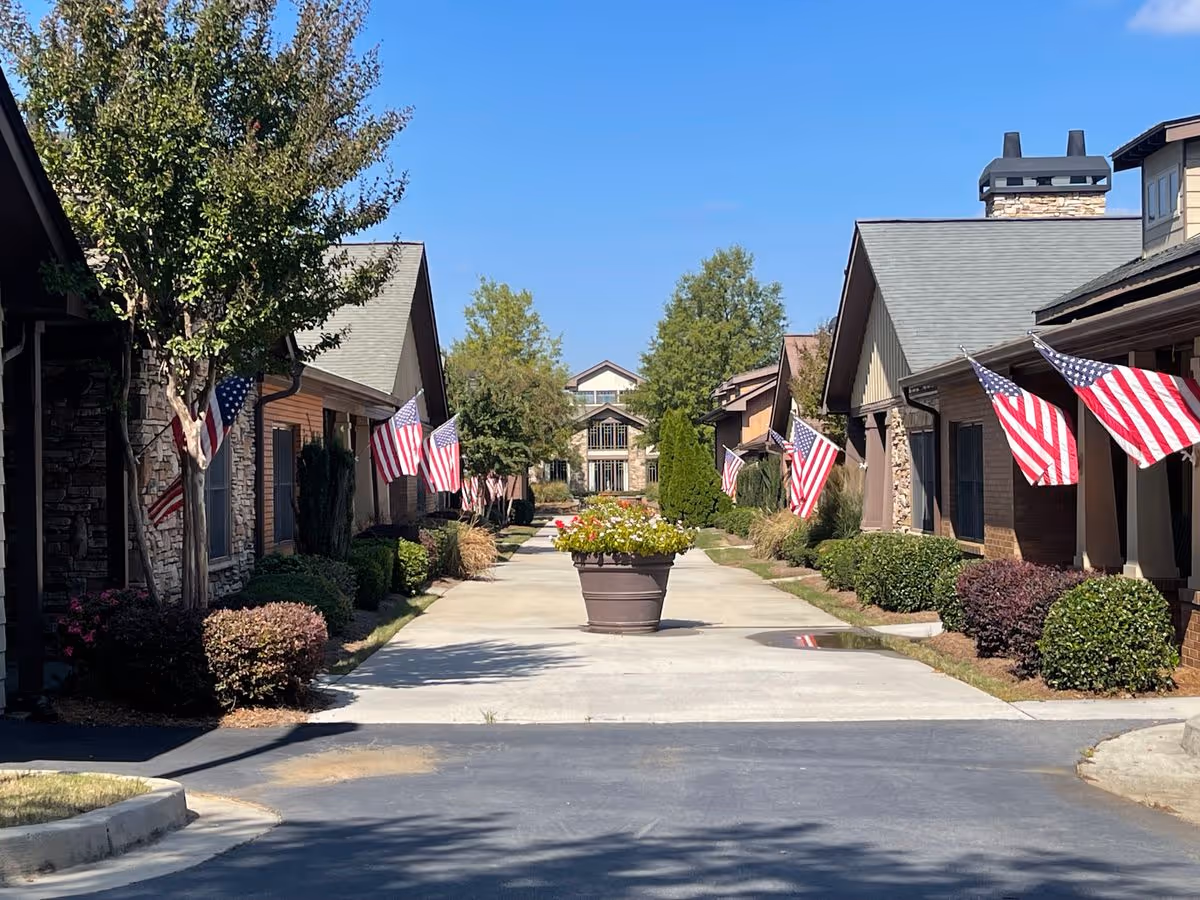 Walkway between single-story buildings lined with American flags and a central planter leading to a larger building under a blue sky.