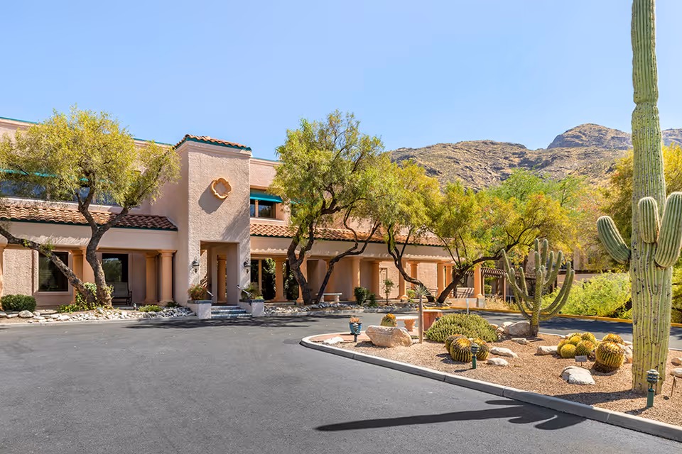Front entrance of a Southwestern-style building with desert landscaping, cacti, and mountains in the background.