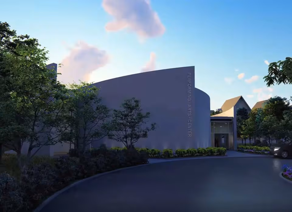 Curved modern performing-arts building entrance with trees, landscaping and a driveway at dusk.