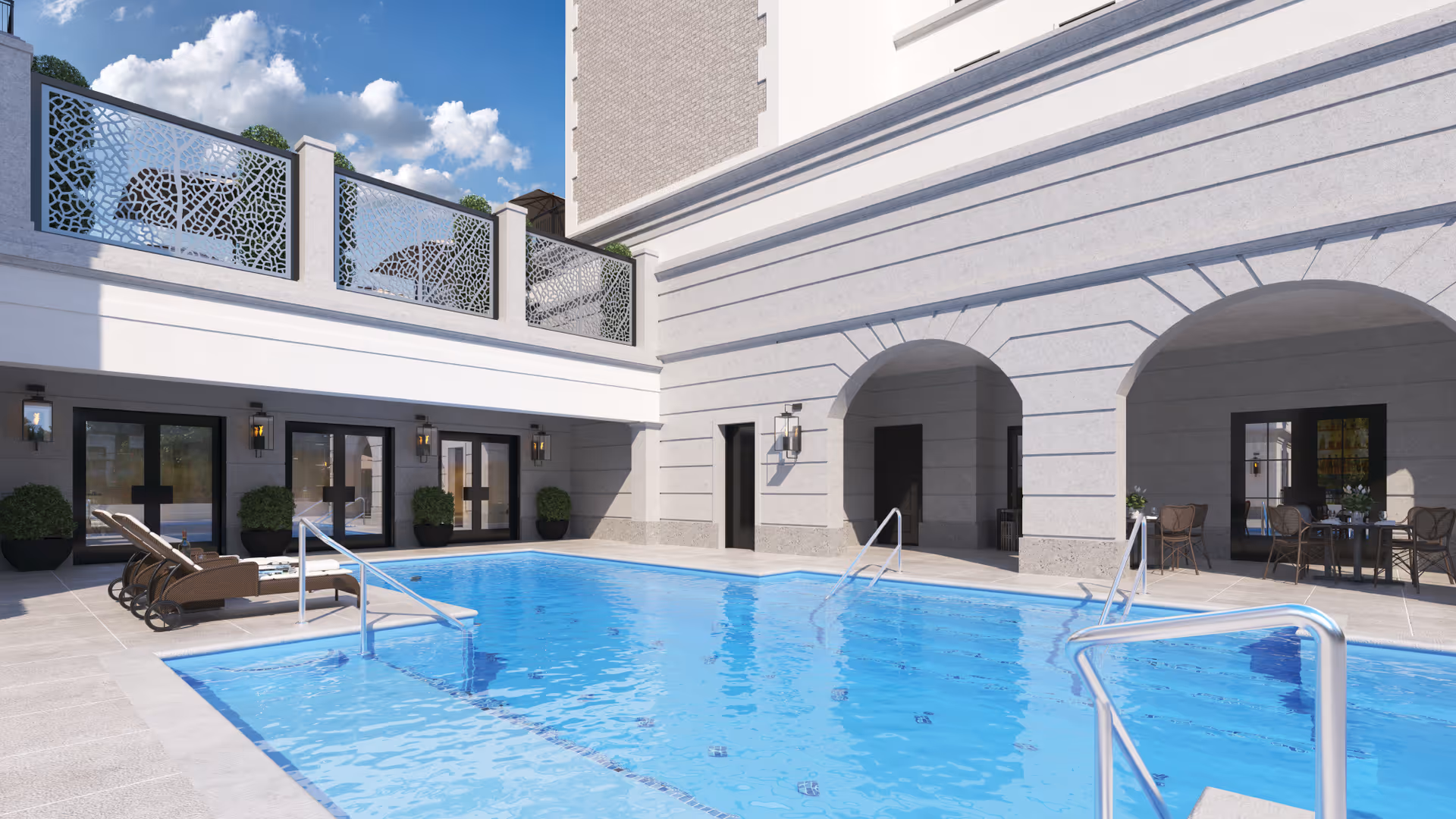 Outdoor swimming pool area at Corso Atlanta with clear blue water, lounge chairs on the left side, potted plants near the building, and a seating area with tables and chairs under an archway on the right side. The building has decorative metal panels on the upper level and a partly cloudy sky overhead.