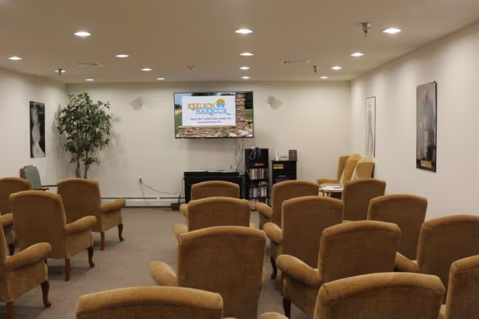 A small common room with rows of upholstered armchairs facing a wall-mounted TV showing the Keelson Harbour logo.