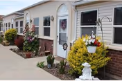 Front entrance of a single-story retirement community building with doors, windows, hanging baskets and decorative planters along a paved walkway.