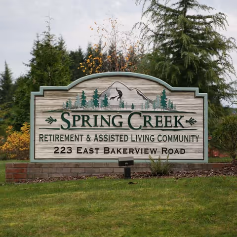 Entrance sign for Spring Creek Retirement & Assisted Living Community with the address displayed, set on a brick base and landscaped lawn.