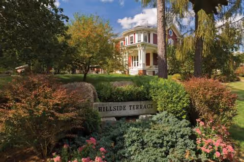 Hillside Terrace exterior with a stately porch, lush landscaping, and a garden sign.