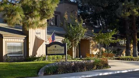 Exterior view of Atria Willow Glen facility with flag, sign, and landscaped entrance.