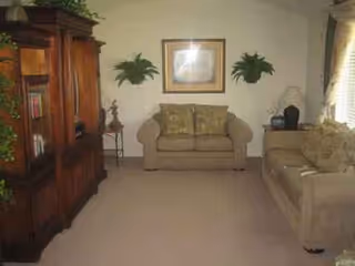 A cozy living room with beige sofas, wooden cabinet, and framed wall art