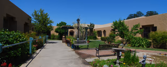 Sunny courtyard with benches, walkways, landscaping and a single-story stucco building surrounding it.