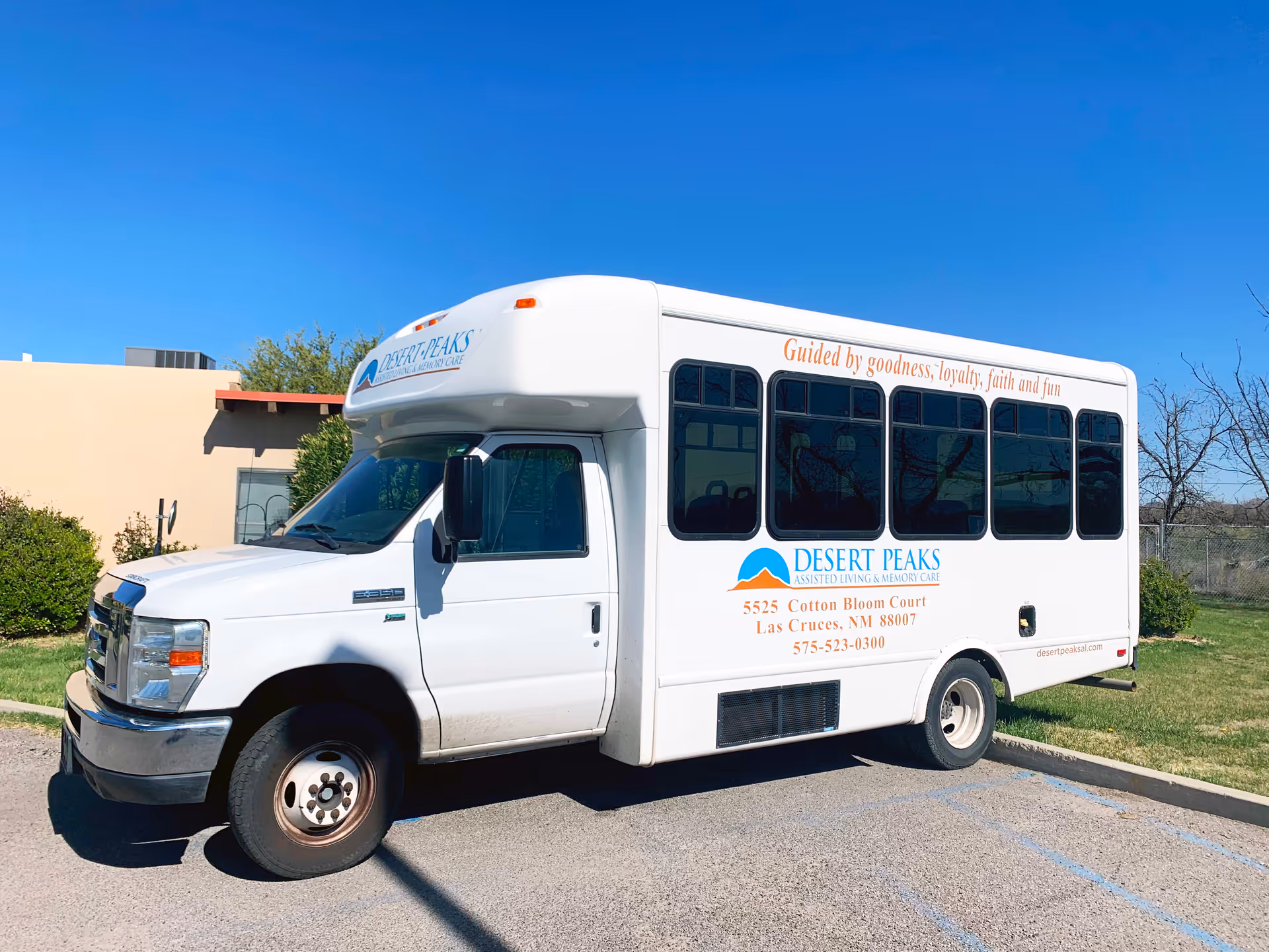 White Desert Peaks Assisted Living shuttle bus parked outside a building under a clear blue sky.