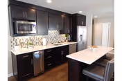 Modern kitchen with dark wood cabinets, stainless steel appliances, a center island with seating, and a patterned tile backsplash.