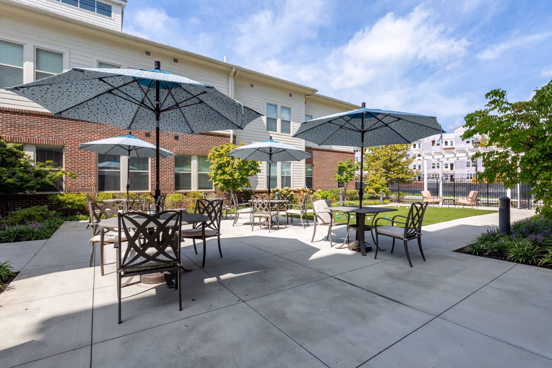Outdoor courtyard patio with several tables, chairs, and blue umbrellas beside a multi-story brick-and siding building.