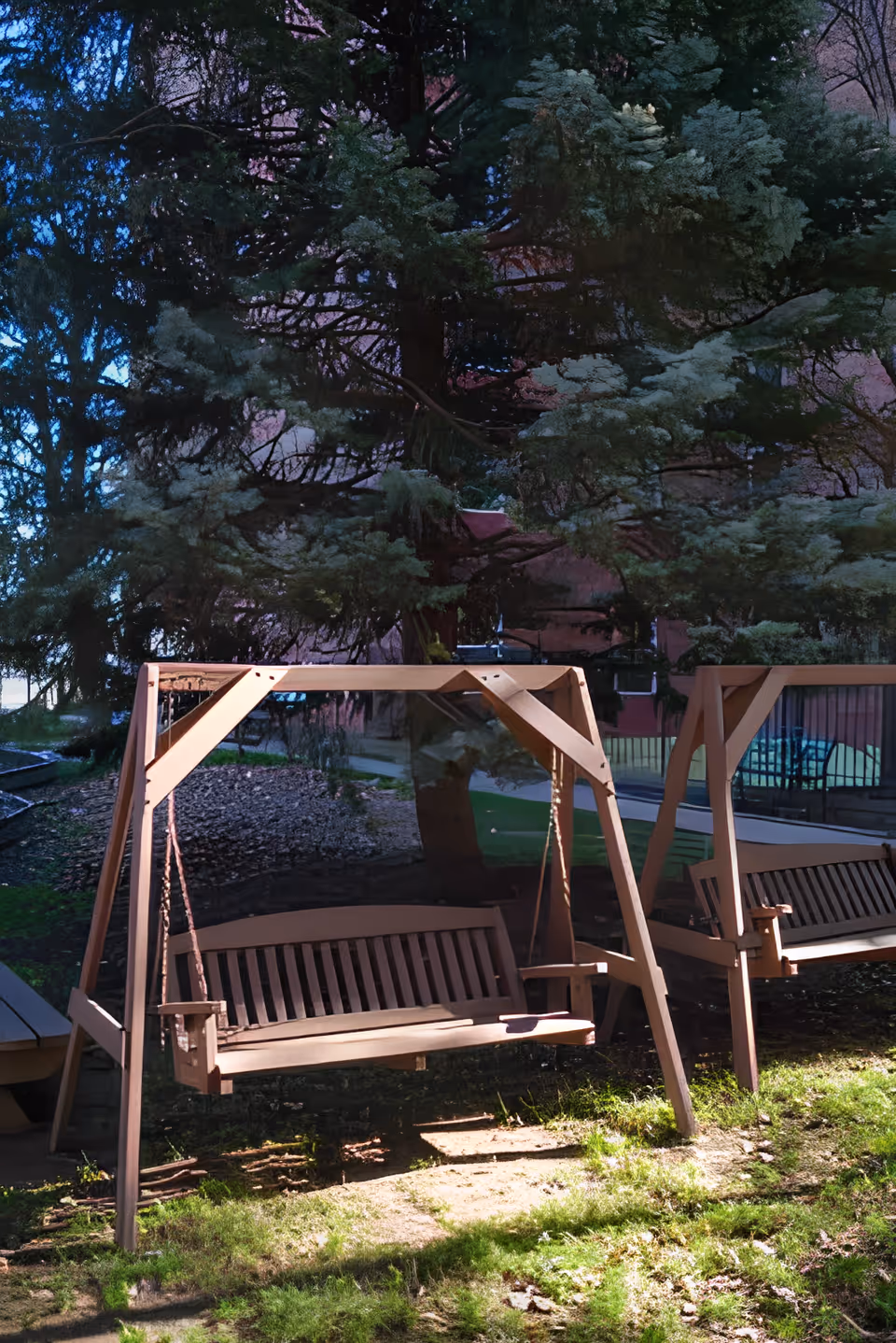 Two wooden porch swings hanging from wooden frames in an outdoor garden area with grass and trees in the background.