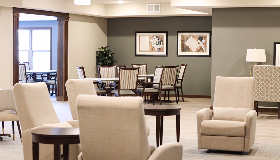 Open communal dining and lounge area with upholstered armchairs, round tables, and dining chairs.
