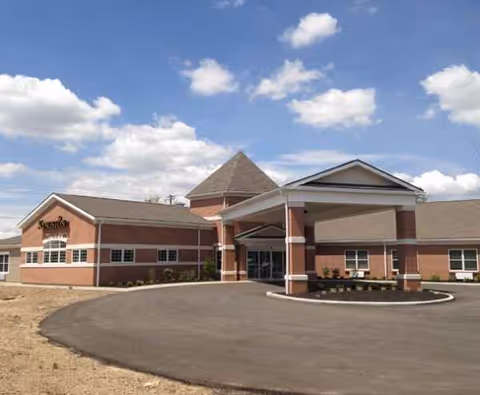 Brick senior living facility with a covered entrance and circular driveway under a blue sky.