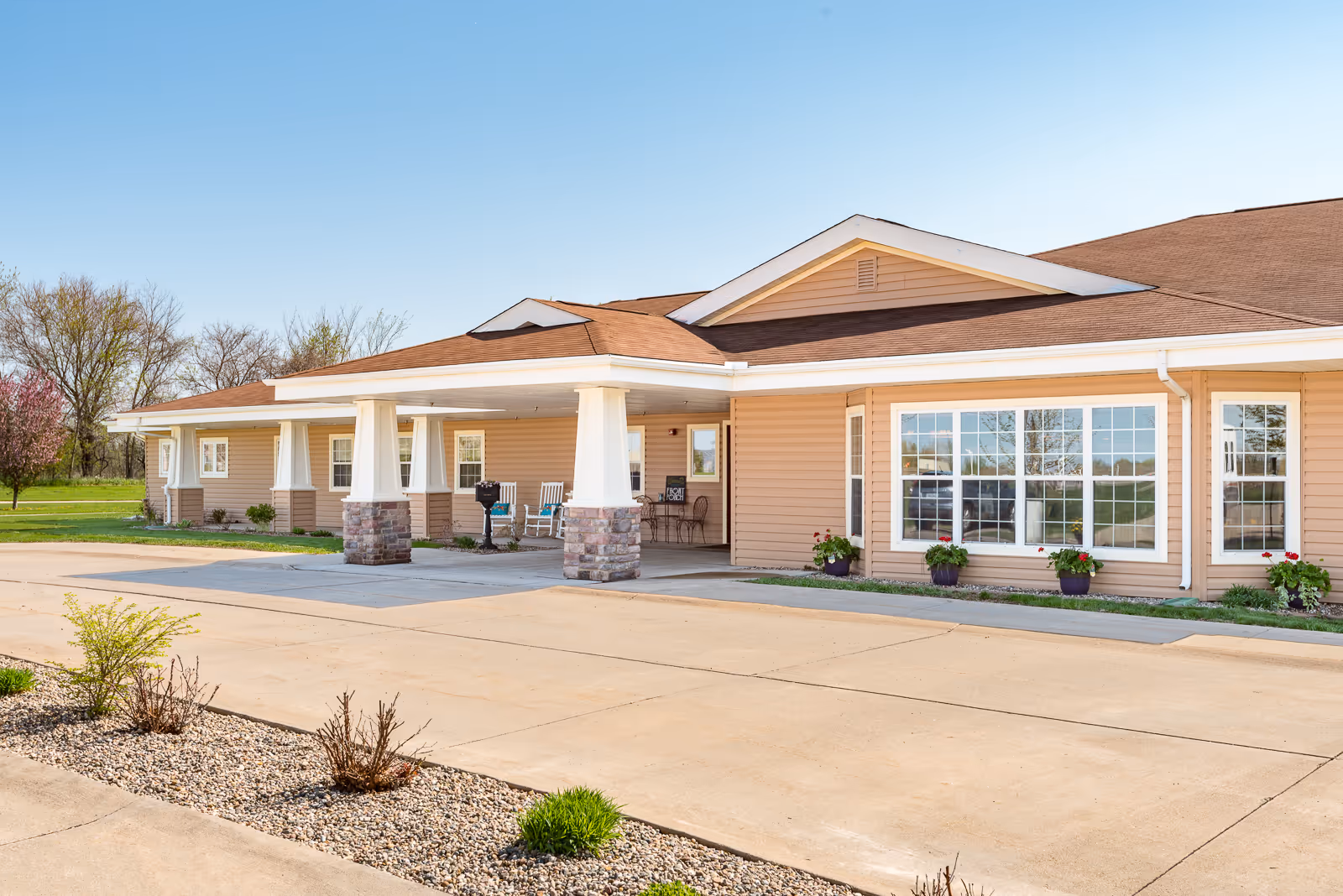 Front exterior of a single-story beige senior living facility with a covered entrance, columns, and large windows.