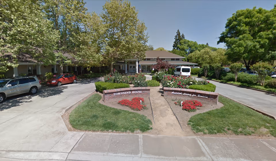 Front exterior of Townsend House assisted living facility showing the entrance, landscaped flowerbeds, and a circular driveway.