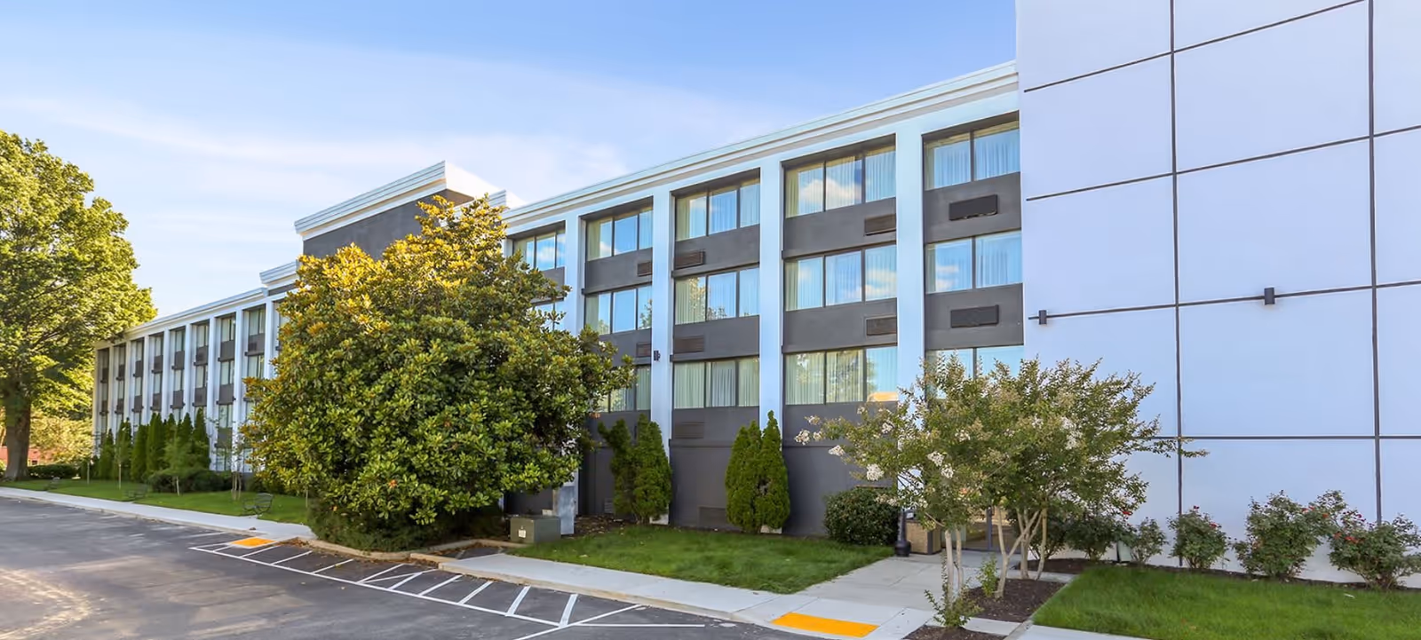 Front exterior of the Silverleaf Senior Living building with multiple rows of windows, parking spaces, and landscaped trees and shrubs.