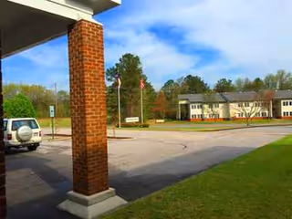 Outdoor view of a parking lot, flagpoles, and a distant building beyond a covered entrance.