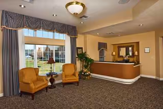 Lobby seating area with two orange chairs, lamp, curtains, and a reception desk.