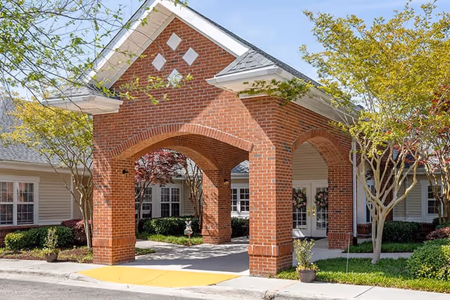 Covered brick porte-cochère entrance to a residential building with arched openings and landscaped trees.