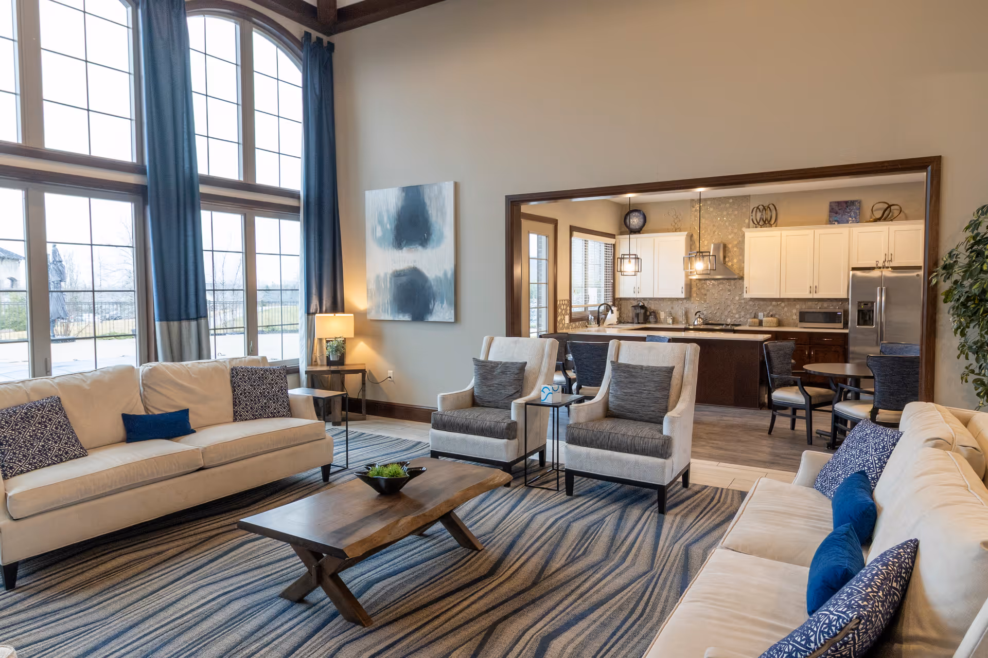 Bright, spacious living room with large arched windows, sofas and armchairs around a wooden coffee table and an open view into the kitchen.