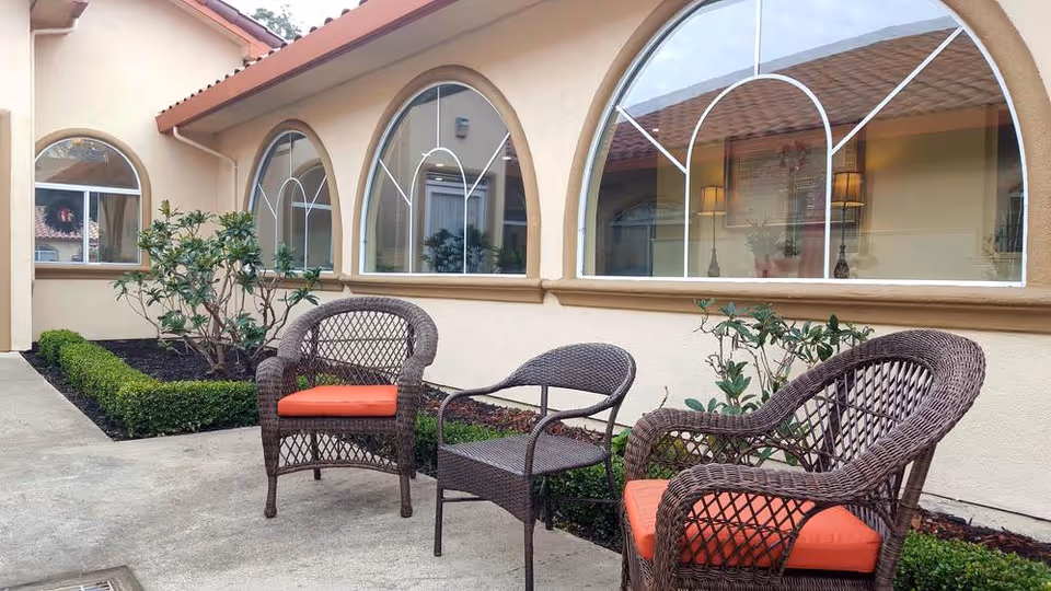 Outdoor courtyard with wicker chairs topped by orange cushions on a concrete patio in front of arched windows.