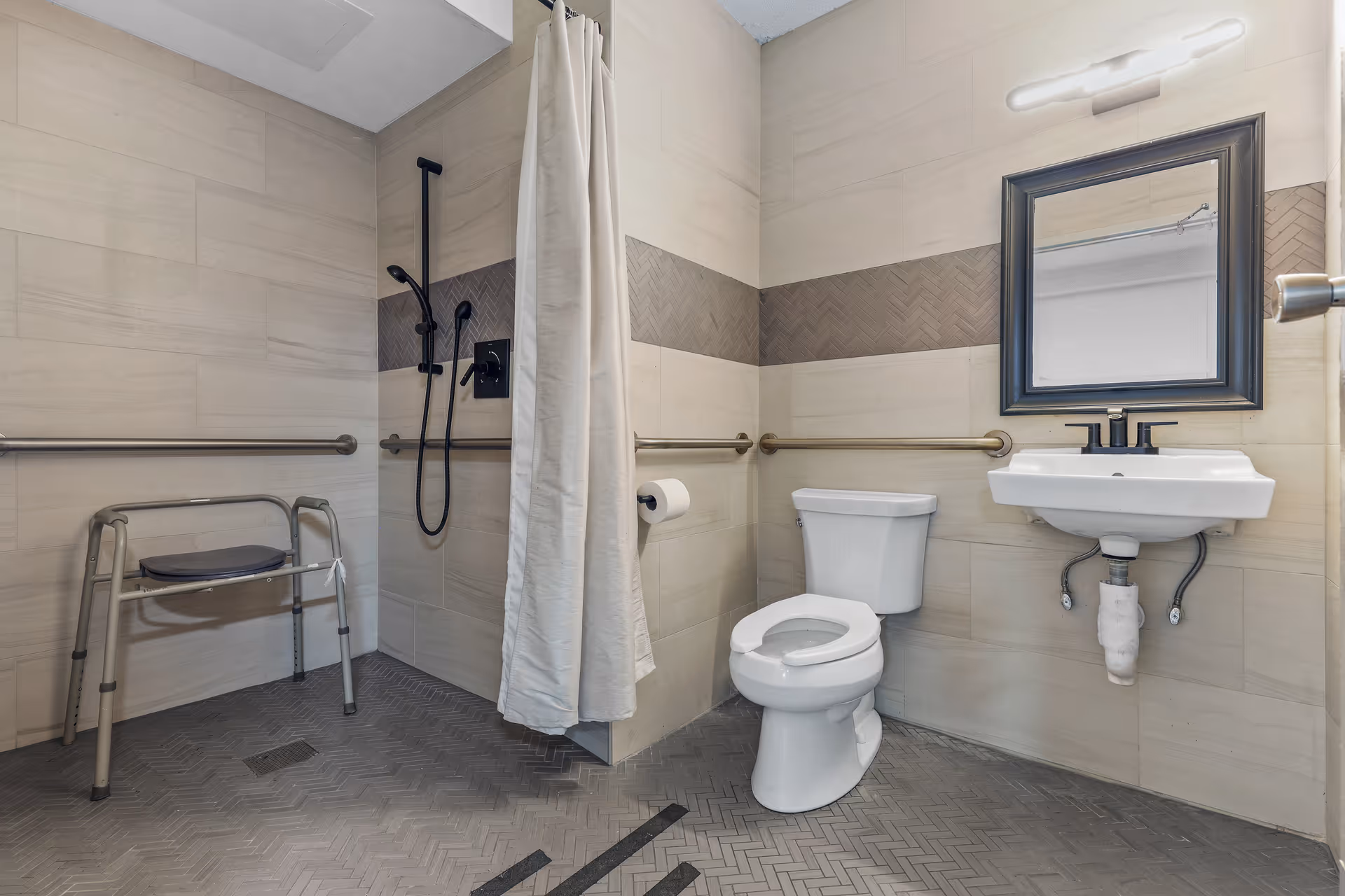 Accessible bathroom with a toilet, wall-mounted sink, grab bars, and a shower area with a curtain and shower chair.