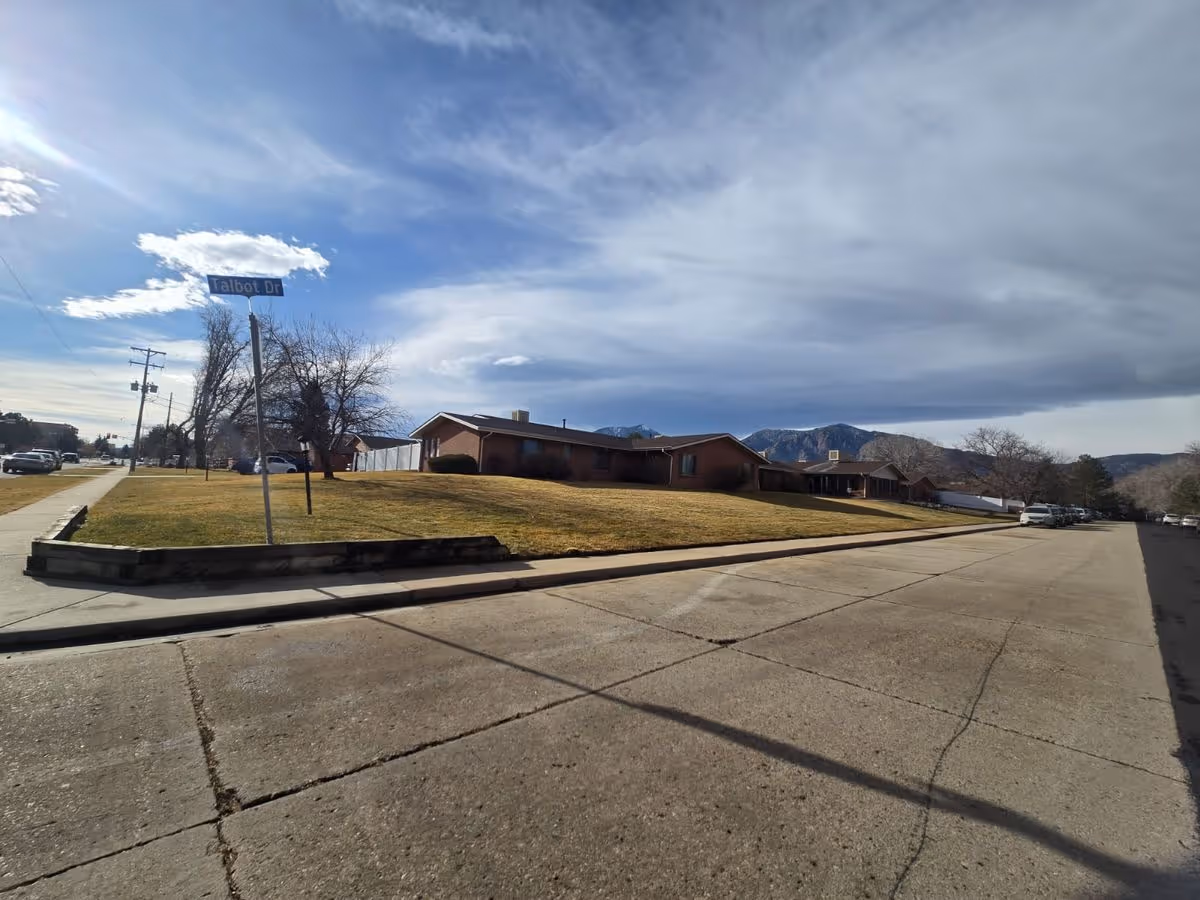 Single-story brick buildings set back on a grassy lawn beside a street with a 'Talbot Dr' sign under a partly cloudy sky.