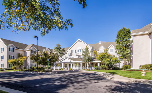 Entrance and front exterior of a multi-story senior living building with a covered driveway, landscaping, and blue sky.
