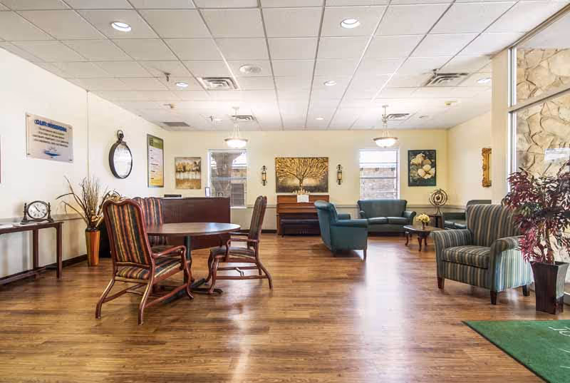 Spacious nursing home common lounge with chairs, sofas, tables, and wall artwork.