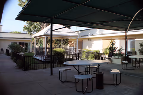 Shaded outdoor courtyard with round picnic tables, a gazebo, and surrounding single-story building.