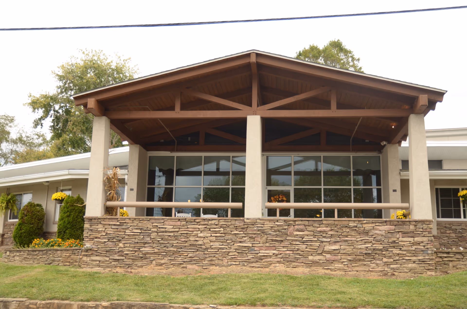 Covered stone-front entrance with a wooden gabled porch and large glass windows on a single-story building.