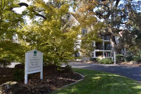 Front exterior of O'Connor Woods senior living with a sign, driveway, and trees.