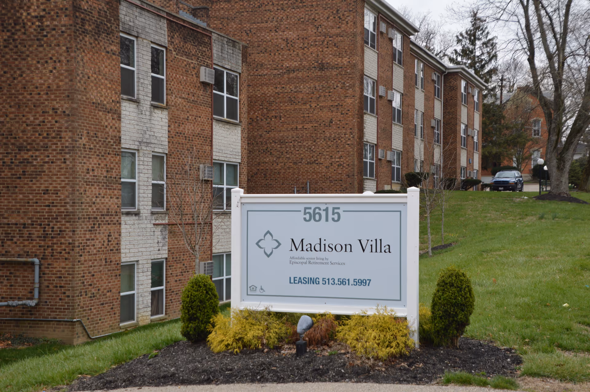 A sign for "Madison Villa" on a lawn in front of a multi-story brick apartment building.
