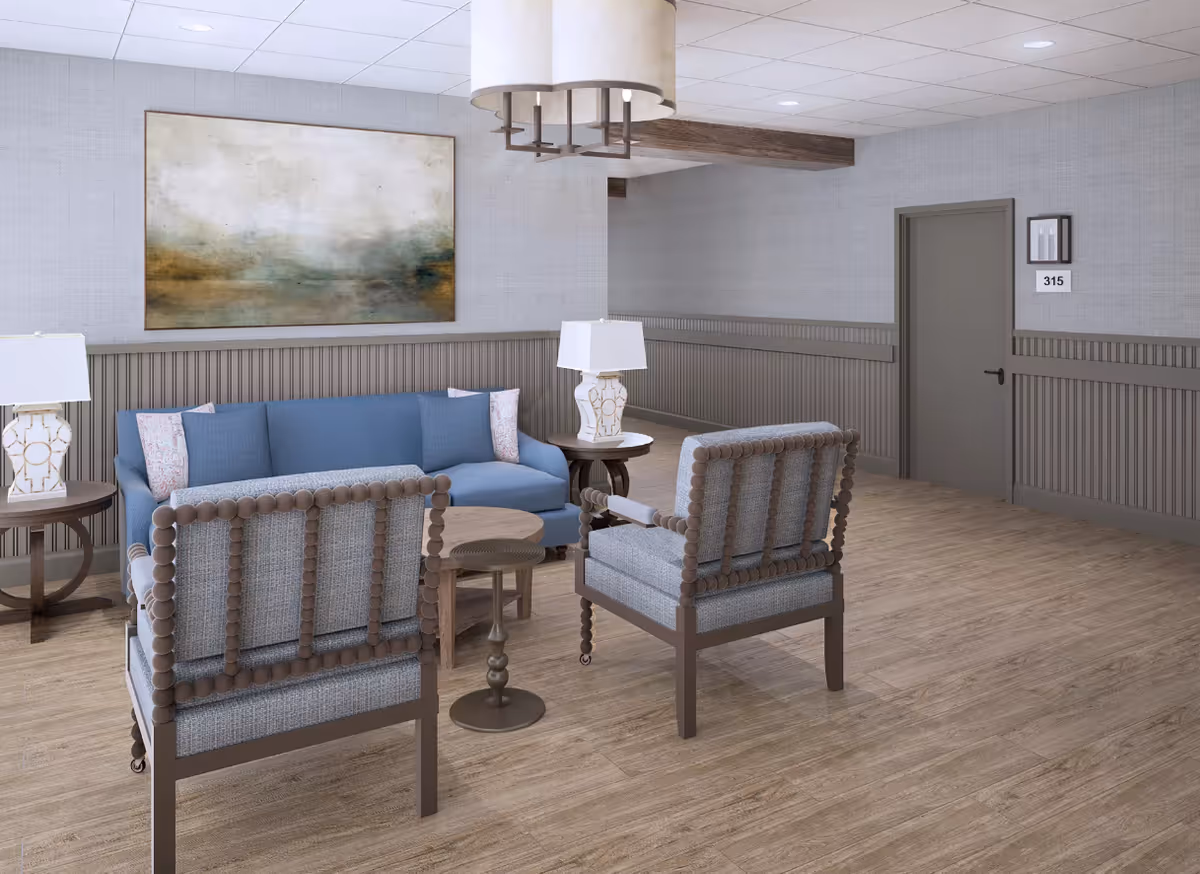 A lounge seating area with a blue sofa, two upholstered chairs, side tables and lamps against a gray paneled wall.