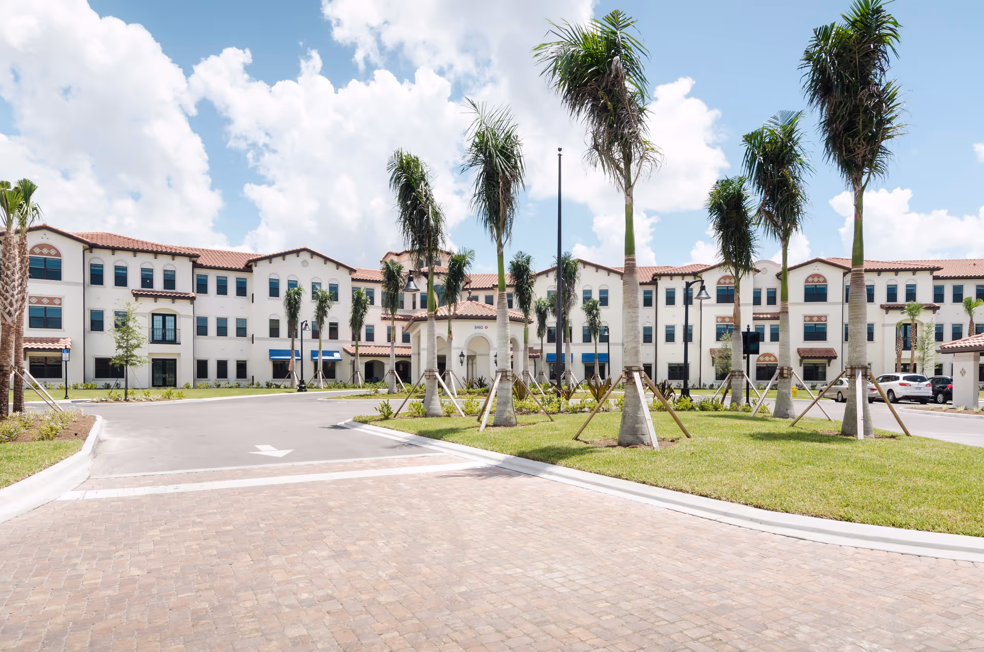 Front exterior of a three-story Mediterranean-style senior living building with palm trees and a circular driveway.